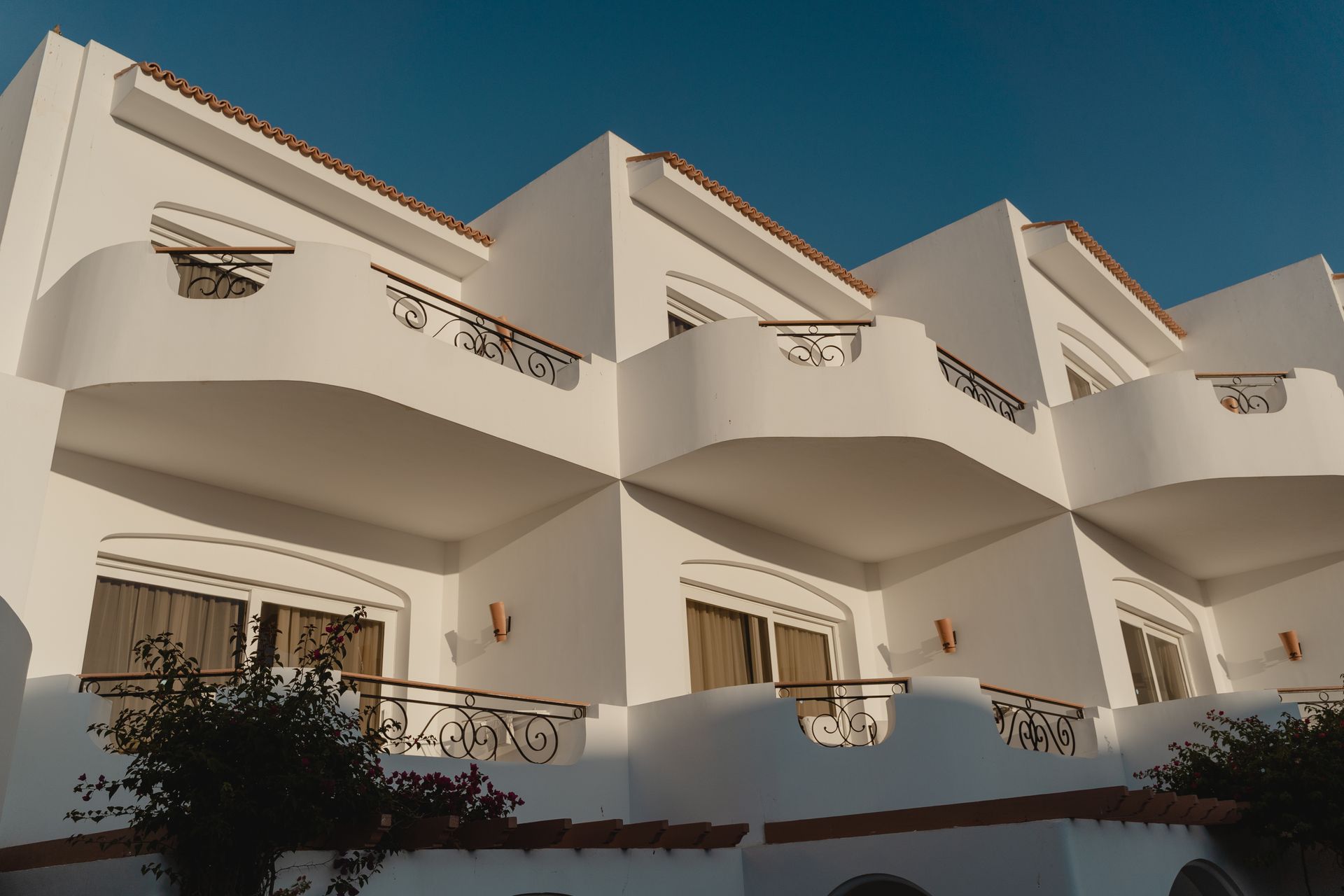 Fachada de hotel mediterráneo bajo, blanco, con balcones de forja